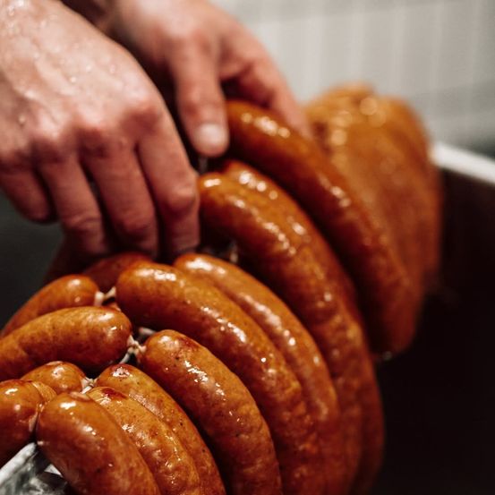 Eine Nahaufnahme der Hände einer Person, die mehrere Würste in einem Behälter hält, möglicherweise zur Zubereitung zum Kochen.