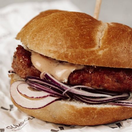 Ein Nahaufnahme eines Fleischpatty-Sandwichs mit cremiger Sauce und geschnittenen roten Zwiebeln auf einem Brötchen, auf weißem Papier platziert.