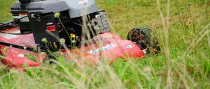 Ein roter Rasenmäher mit schwarzem Motor und grauem Griff liegt im hohen Gras.