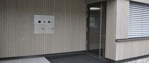 Der Eingang eines Gebäudes mit einer Glastür und einem Teppich davor, die Wand besteht aus Holz, und es gibt ein Schild mit dem Text Dr. Susanne Linda.