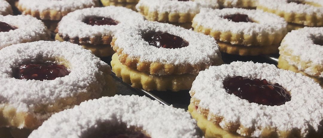 Ein Tablett mit frisch gebackenen Keksen, überzogen mit einer Schicht Puderzucker und gefüllt mit roter Marmelade. Die Kekse sind rund und leicht abgeflacht und ordentlich auf einem Kühlgitter angeordnet.