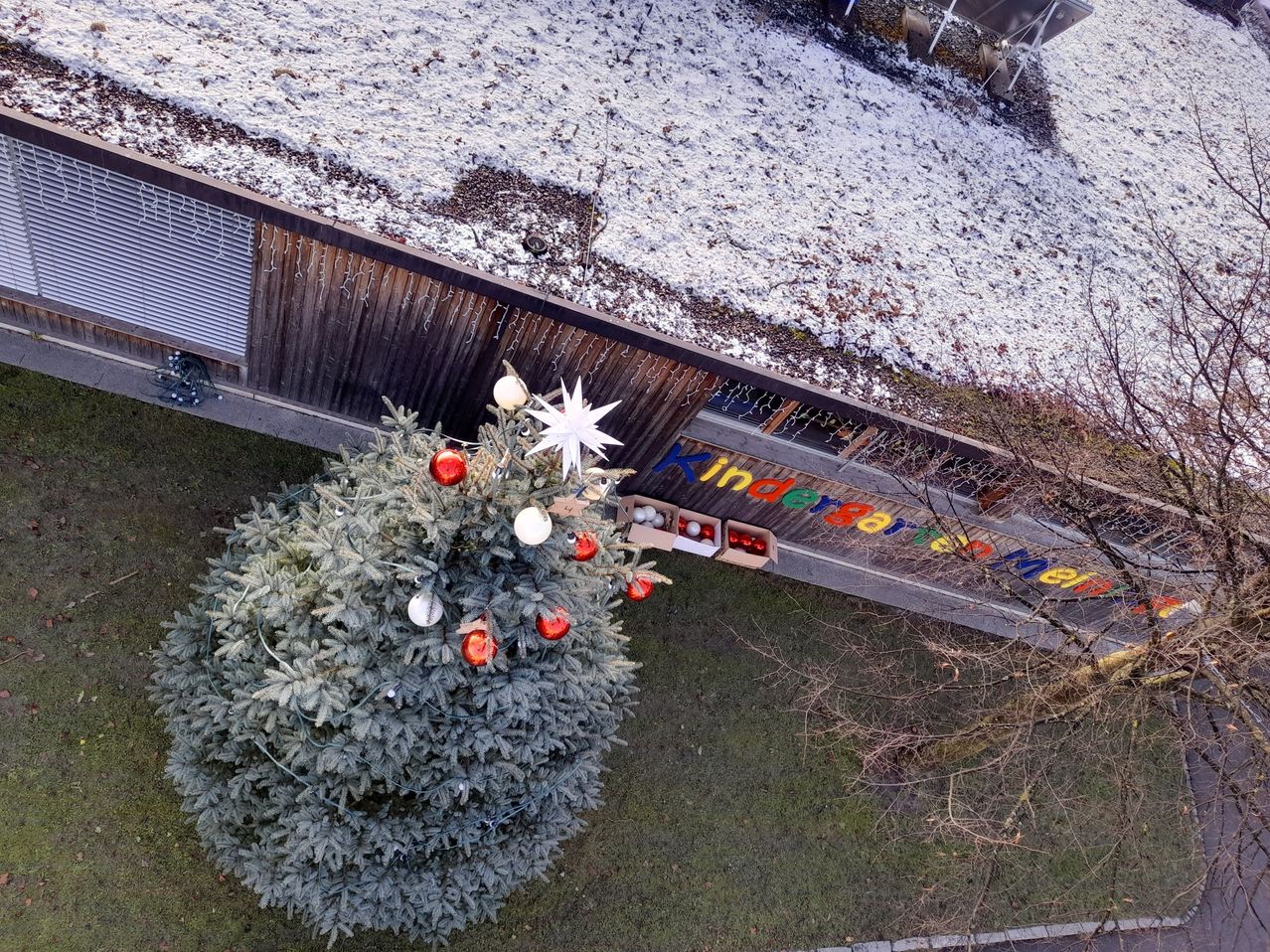 Ein Luftbild eines Weihnachtsbaums steht vor einem Gebäude mit schneebedecktem Dach und einem Schild, das Kinderbarren Neu besagt.