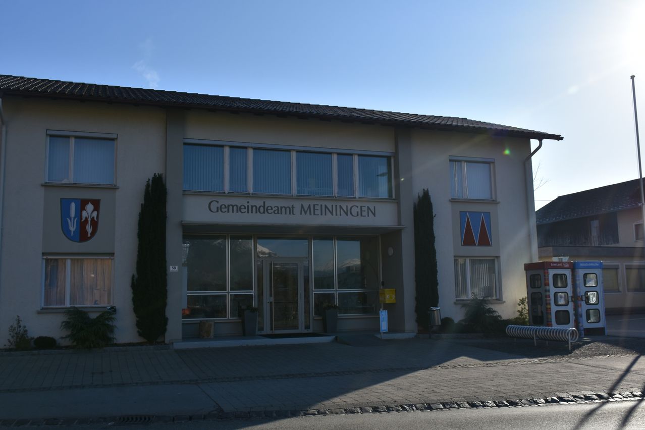 The entrance of the town hall in Meiningen, Germany, features large glass windows, a glass door, and a sign with the town's name.