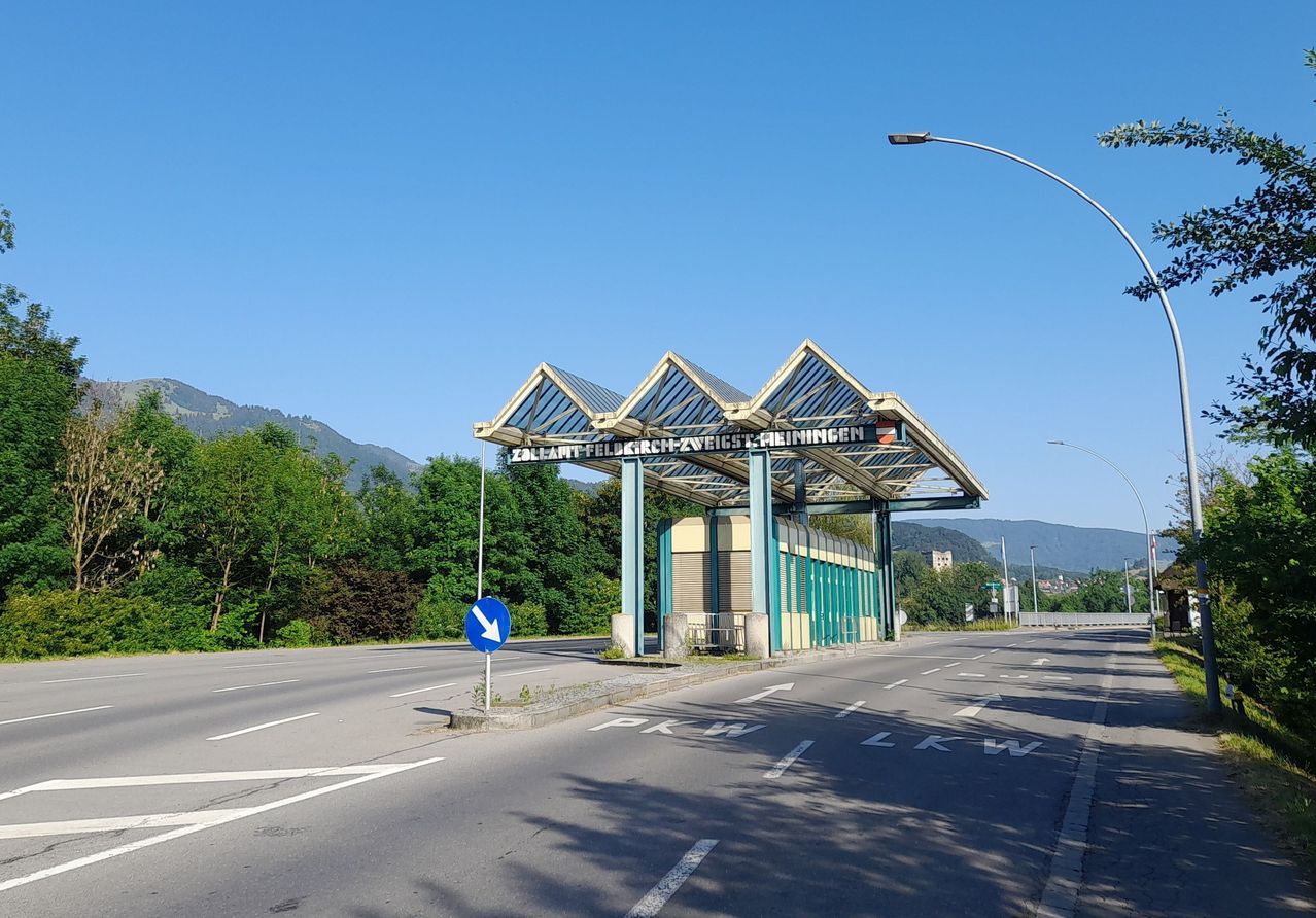 Eine Straßenunterführung mit einem Schild, das 'Zallant-Feldkirch-Zweigs-Meiningen' liest. Die Straße ist leer mit Grün und Bergen in der Ferne.