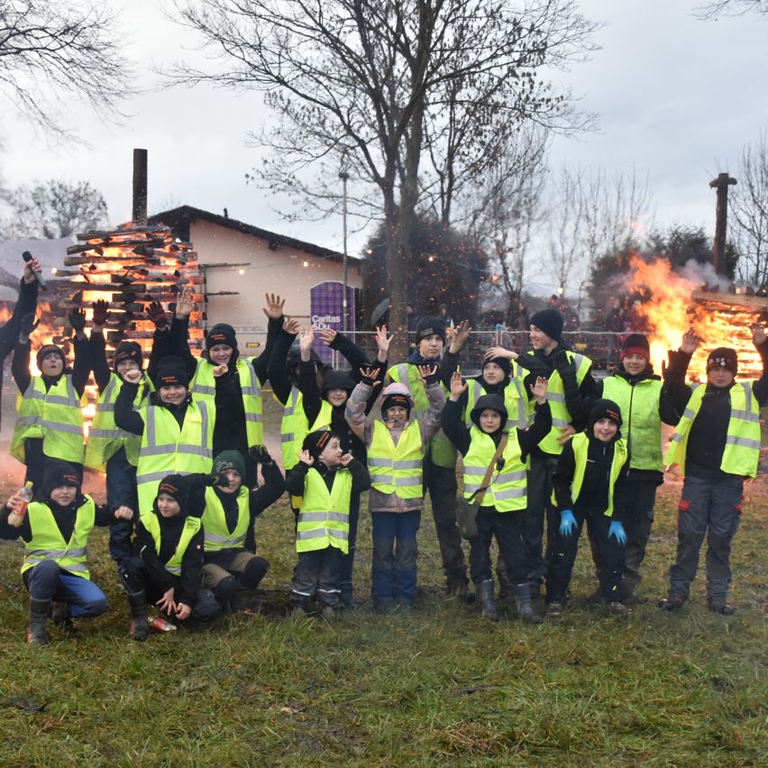 Eine Gruppe von Kindern in gelben Warnwesten posiert für ein Foto vor einem brennenden Lagerfeuer an einem Wintertag.