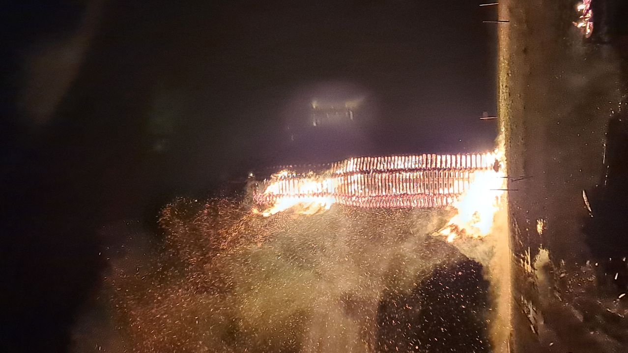 Ein Lagerfeuer brennt nachts hell, mit Funken, die in den dunklen Himmel fliegen. Das Feuer besteht aus Holz, das in einer Reihe angeordnet ist.