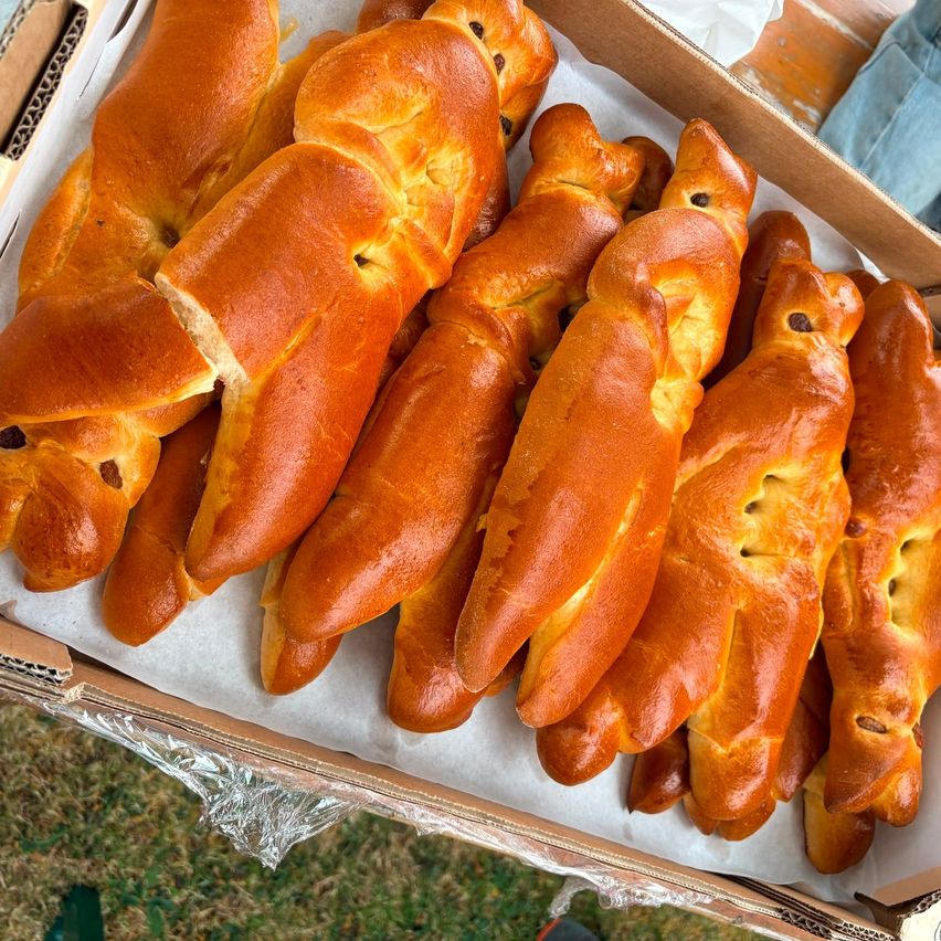A box of freshly baked, golden-brown braided bread with dark fillings, displayed on a wooden surface.