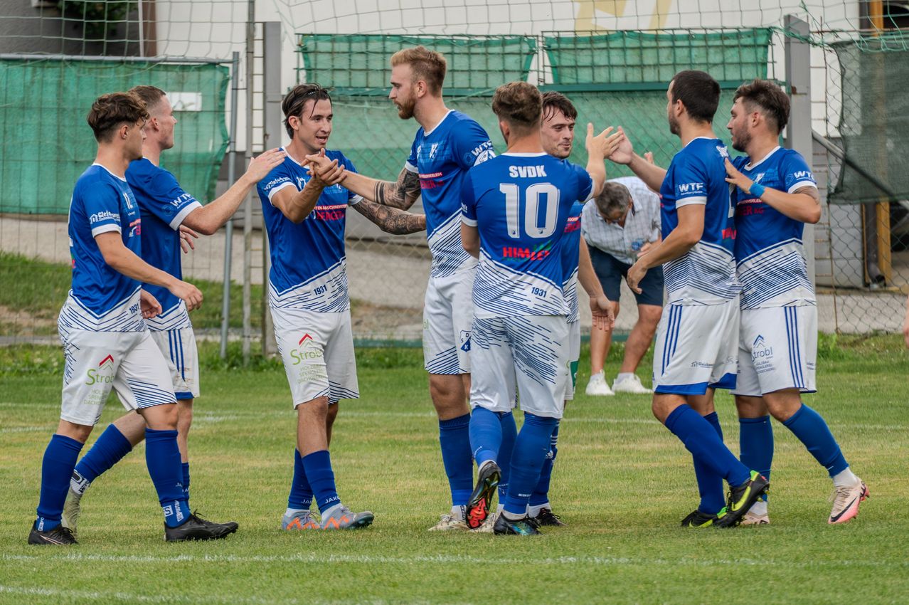 Fußballspieler feiern einen Sieg auf einem Feld in blauen Trikots. Ein Spieler trägt ein blaues Trikot mit der Nummer 10.