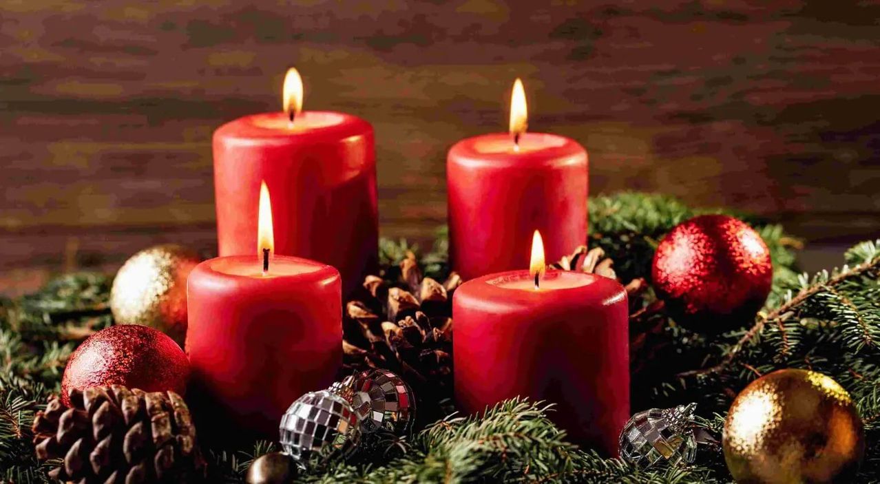 Vier rote Kerzen mit Tannenzapfen und Weihnachtskugeln um sie herum brennen auf einer Holzoberfläche.