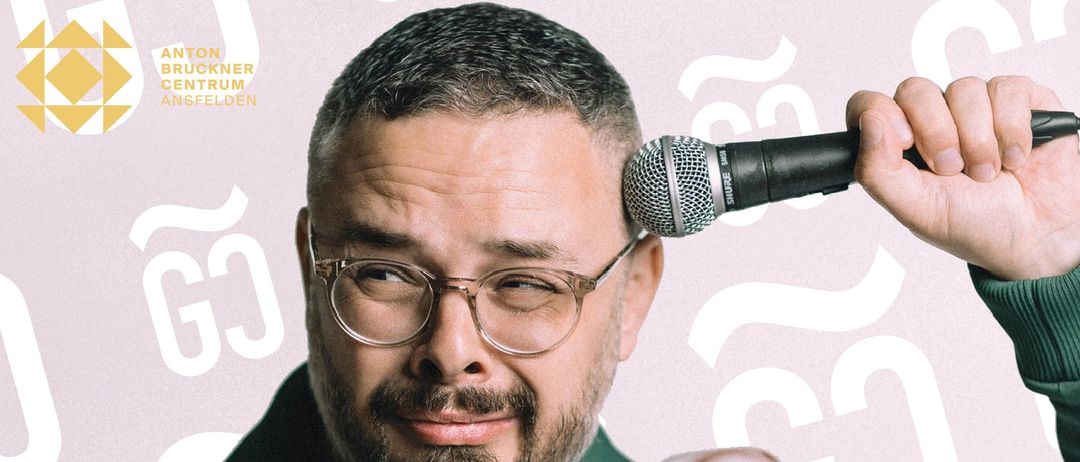 Ein Mann mit Brille und Bart lächelt in die Kamera. Er trägt ein grünes Poloshirt und hat ein Mikrofon auf dem Kopf.