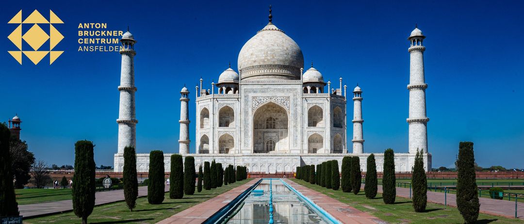 Der Taj Mahal, ein weißes Marmormausoleum, steht majestätisch vor einem klaren blauen Himmel. Es verfügt über eine große Kuppel, Minarette und kunstvolle Schnitzereien.