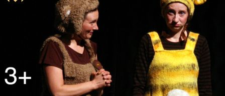 Zwei Frauen in Kostümen, eine mit einem Bärenhut und die andere mit einem Bienenhut, stehen vor einem dunklen Hintergrund.