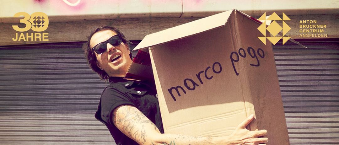 Ein Mann mit Sonnenbrille und schwarzem Shirt hält eine Box mit der Aufschrift 'Marco P'. Er scheint laut zu schreien oder zu sprechen.