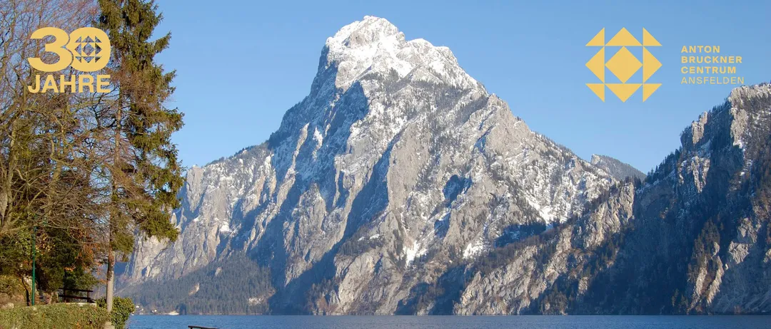 Ein Berg mit Schnee auf seinem Gipfel und felsiger Oberfläche mit einem Gewässer darunter unter einem klaren Himmel.