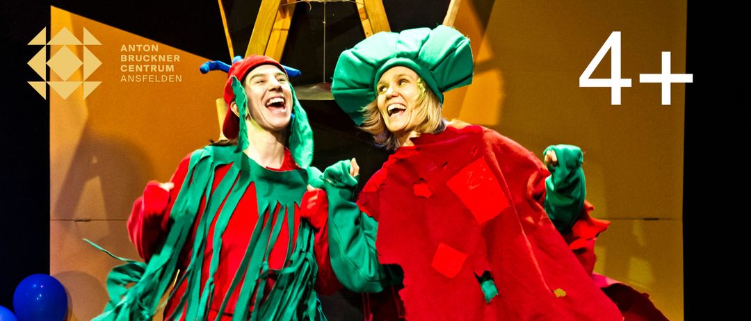Zwei Menschen in Weihnachtskostümen lachen und halten Händchen. Die Person auf der linken Seite trägt einen roten und grünen Hut, und die Person auf der rechten Seite trägt einen grünen Hut.