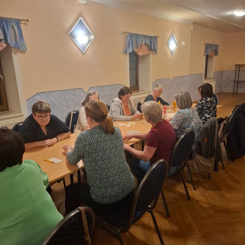 Eine Gruppe von Frauen versammelt sich um einen Tisch in einem Raum, wahrscheinlich für eine Besprechung. Sie sitzen auf Stühlen und einige haben Gläser und Karten auf dem Tisch.