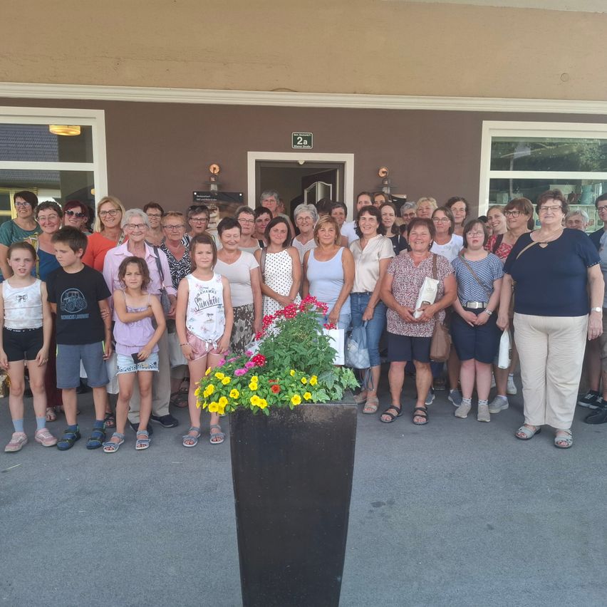 A group of people, including adults and children, are posing for a photo in front of a building with a large planter and flowers.