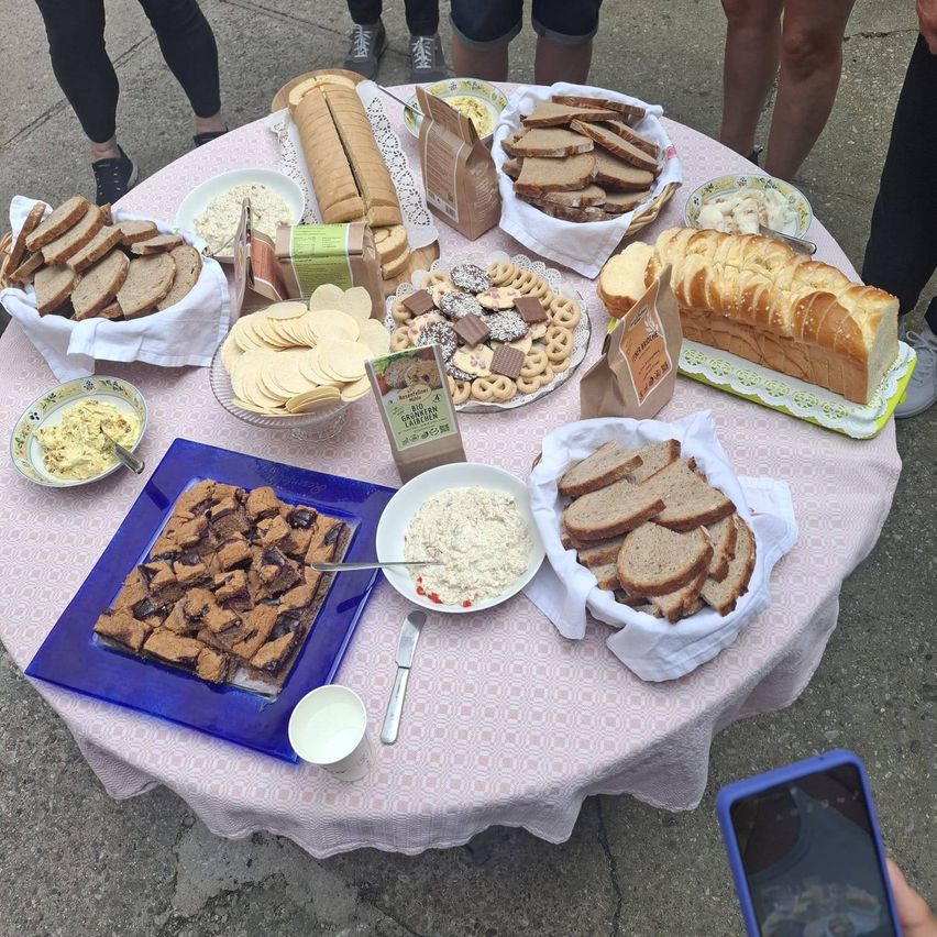 A table with a variety of breads, cookies, and dips, surrounded by people in casual clothing.