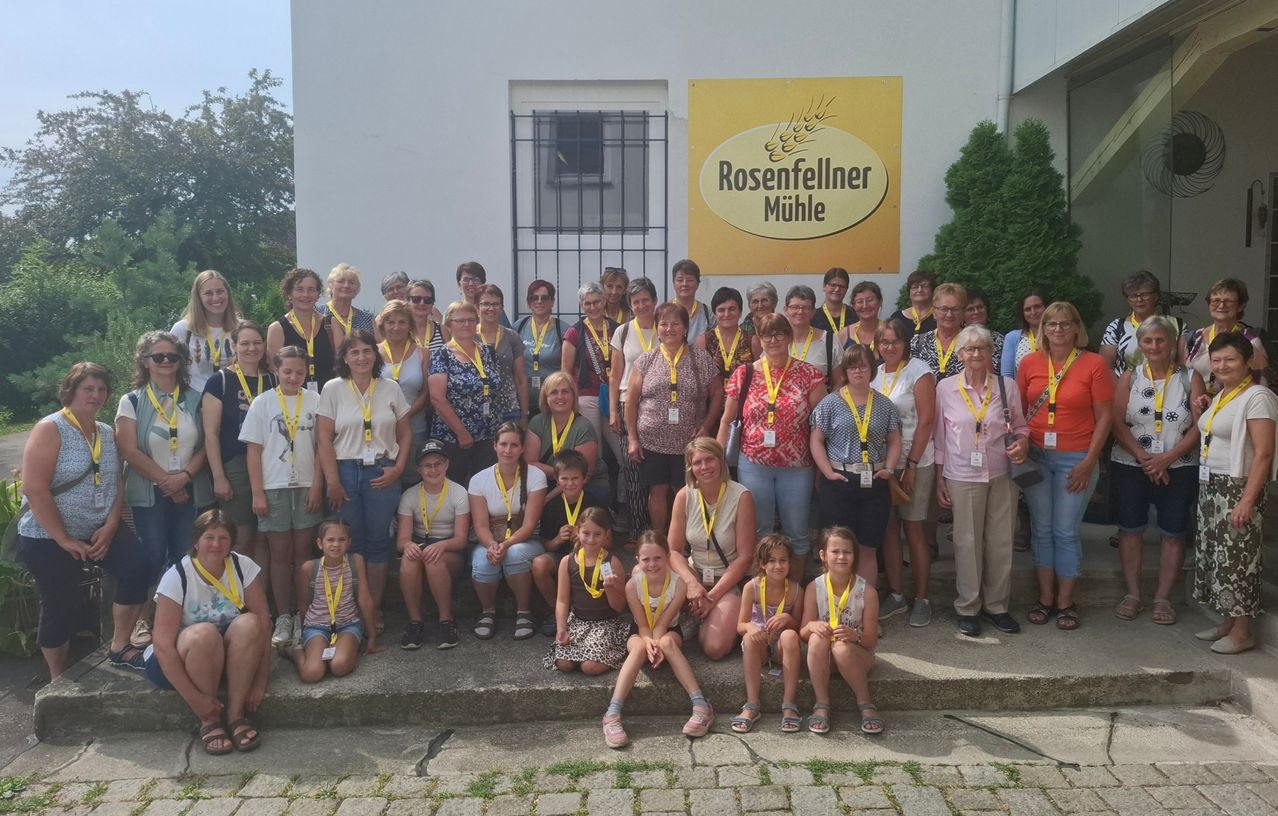 A group of people wearing yellow lanyards are posing for a photo in front of the Rosenfellner Mühle building.