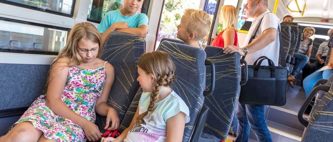 Eine Gruppe von Kindern und Erwachsenen sitzt in einem Bus. Die Kinder sitzen auf blauen Sitzen, und die Erwachsenen stehen.