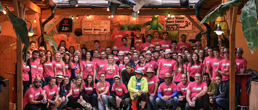 Eine Gruppe von Menschen in rosa T-Shirts posiert für ein Foto in einem überdachten Veranstaltungsbereich mit einem großen Orca, der von der Decke hängt.