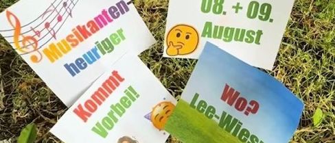 Ein Set bunter Poster mit Nachrichten wie 'Kommt Vorbei!' und 'Lee-Wiesn Wo?' liegen auf dem Gras, mit Noten und einem lächelnden Gesicht.