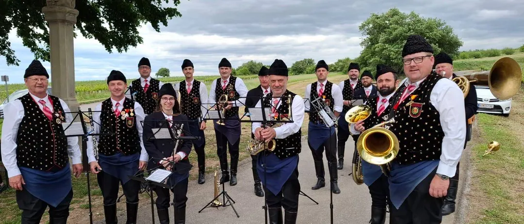 Eine Gruppe von Musikern in traditioneller Kleidung steht auf einem Weg und hält Blechblasinstrumente.