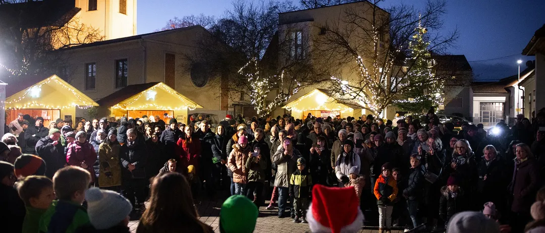 Eine große Menschenmenge versammelt sich bei Nacht vor einer Kirche, viele tragen Winterkleidung und Mützen.