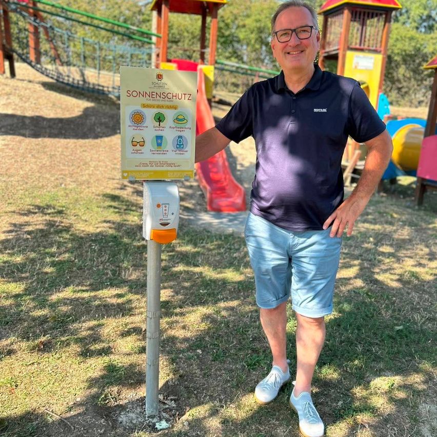 Ein Mann steht neben einem Schild mit Sonnenschutztipps und einem Handdesinfektionsspender auf einem Spielplatz.