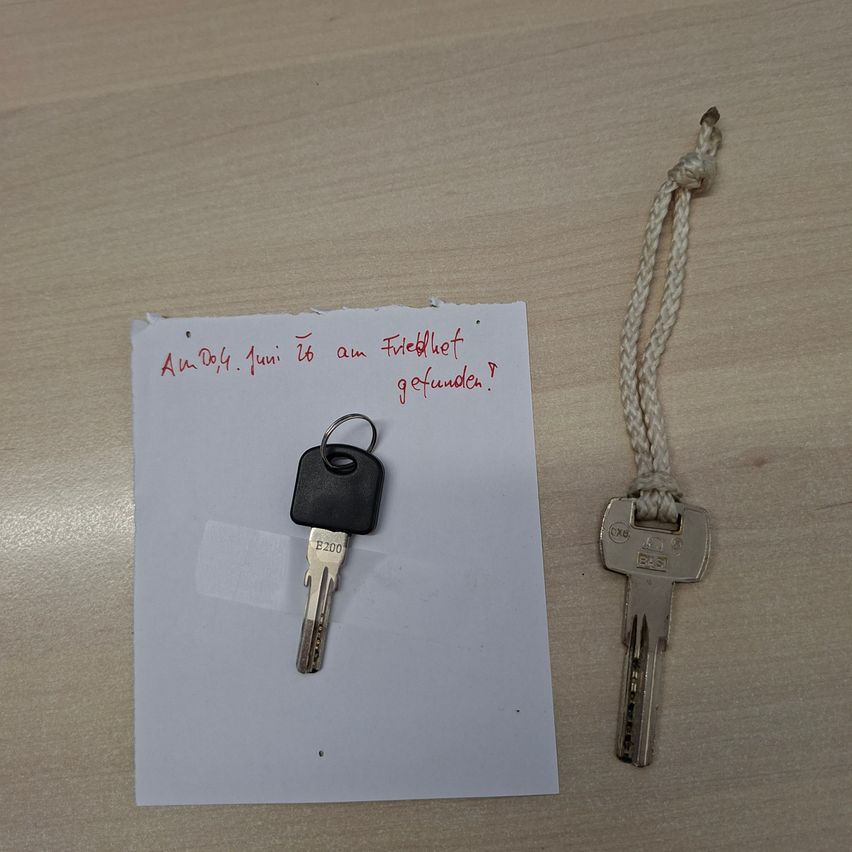 Ein Schlüssel, ein Stück Papier mit fremden Schriftzeichen und ein gebundener Faden liegen auf einer Holzoberfläche.