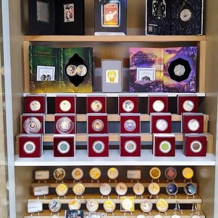 Ein Vitrinenschrank mit mehreren Regalen, gefüllt mit Münzen und Gegenständen in roten und schwarzen Schachteln. Das oberste Regal hat größere Schachteln mit 'Star Trek' und anderen Etiketten. Die mittleren Regale haben Reihen von Münzen in verschiedenen Farben. Das unterste Regal hat größere Münzen, einige mit Etiketten.