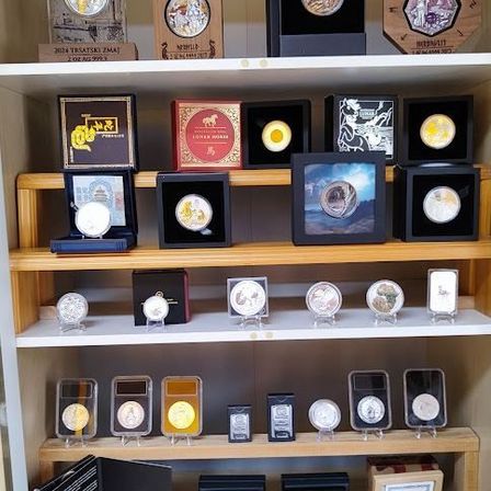 Eine Ausstellung von Sammlermünzen auf Regalen mit verschiedenen Schachteln und Rahmen, die unterschiedliche Designs und Themen präsentieren. Jede Münze befindet sich in einem separaten Halter.