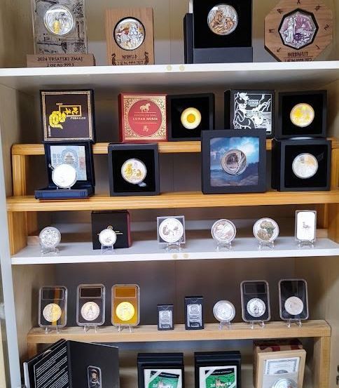 Eine Ausstellung von Sammlermünzen auf Regalen mit verschiedenen Schachteln und Rahmen, die unterschiedliche Designs und Themen präsentieren. Jede Münze befindet sich in einem separaten Halter.