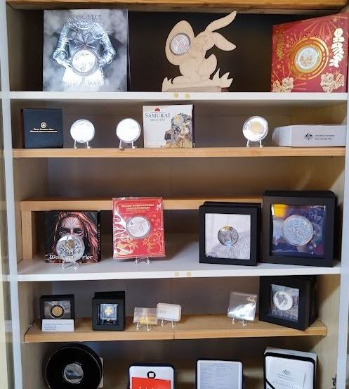 Ein holzfarbenes Regal zeigt verschiedene gerahmte Bilder, Münzen und Schachteln. Eine Münze zeigt einen Samurai, eine andere einen Hasen und andere verschiedene Designs.