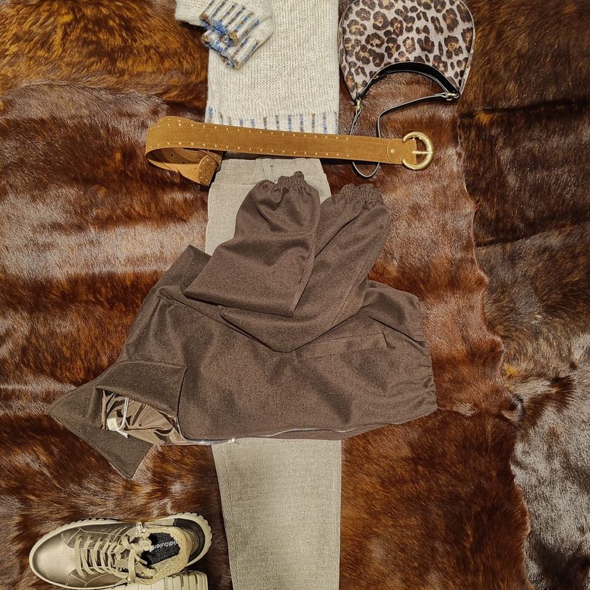 Ein Paar Turnschuhe, ein Gürtel, ein Schal, eine Mütze und eine Hose liegen auf einem braunen Pelztuch.