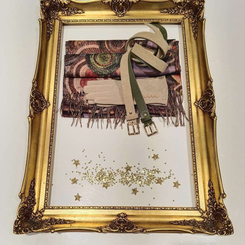Ein goldfarbener Bilderrahmen zeigt ein Tuch, Handschuhe und einen Gürtel. Das Tuch hat Fransen und ein Sternenmuster. Der Hintergrund des Bildes ist mit einem goldenen Sternenmuster verziert.