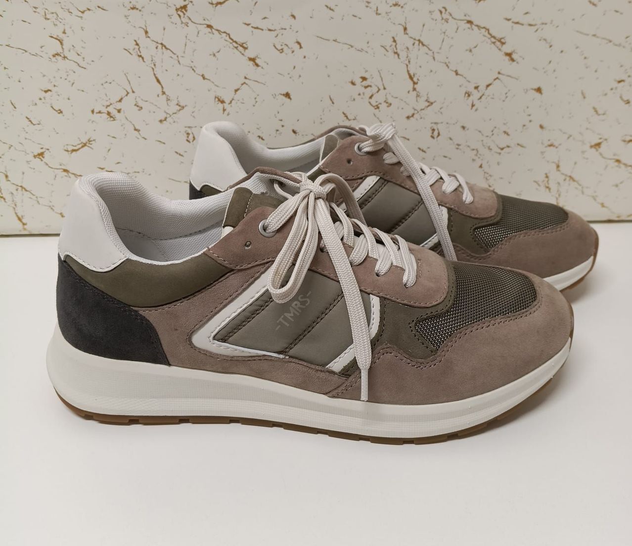 Ein Paar braune und weiße Sneaker mit weißer Sohle und weißen Schnürsenkeln. Die Sneaker stehen auf einer weißen Oberfläche.