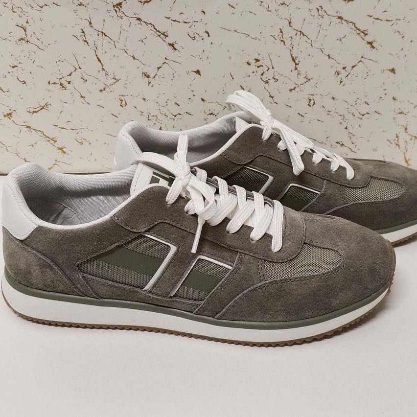 Ein Paar graue Wildleder-Sneaker mit weißen Schnürsenkeln und weißer Sohle vor einem Marmorhintergrund.