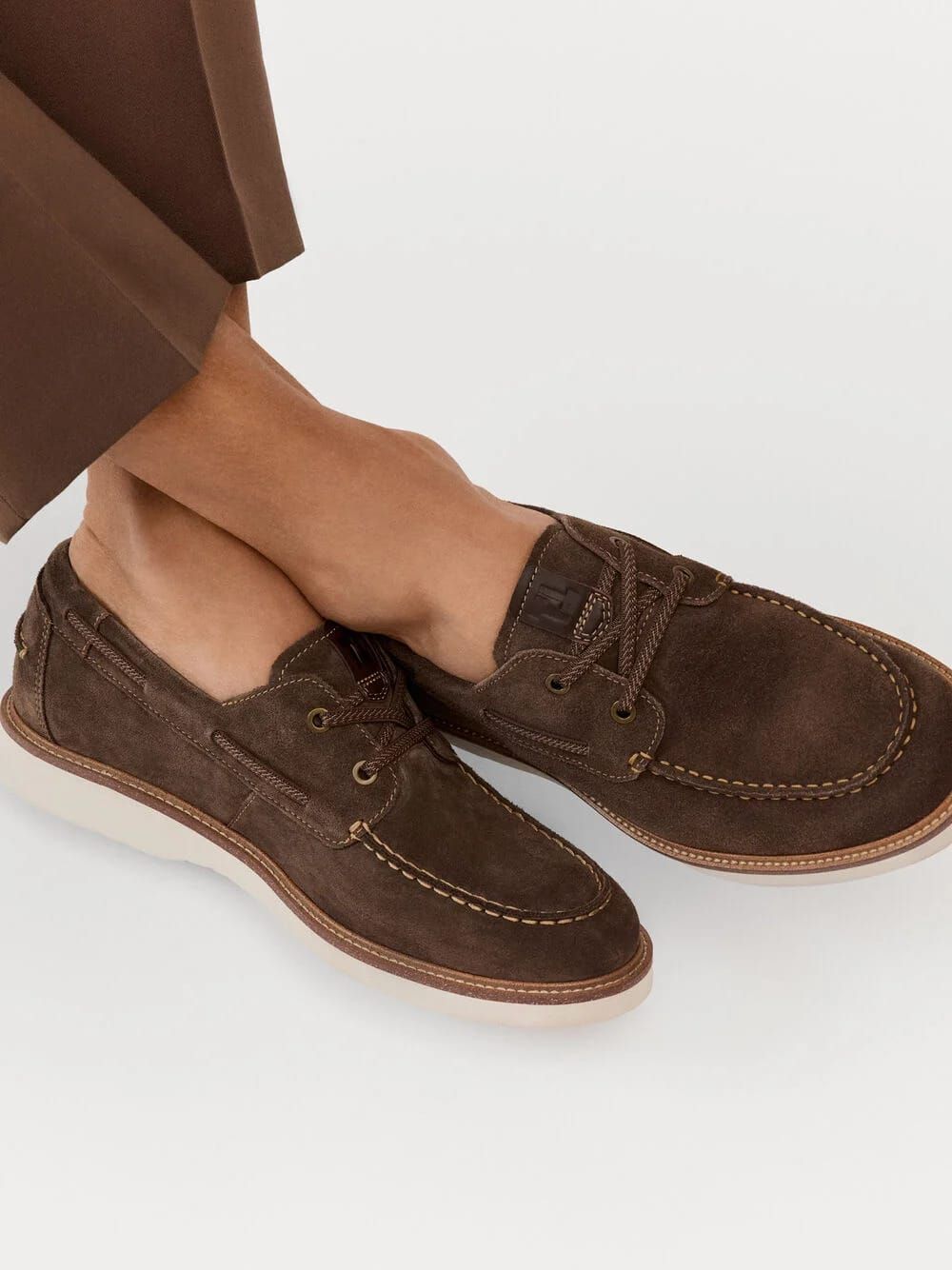 Eine Person trägt braune Wildleder-Loafer mit weißer Sohle. Die Schuhe haben ein klassisches Design mit sichtbaren Nähten und einer braunen Schnürung.