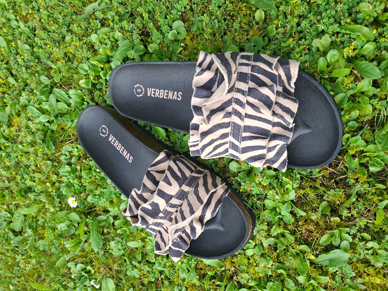 Schwarze Verbenas-Sandalen mit Zebra-Print-Rüschen auf grünem Gras.