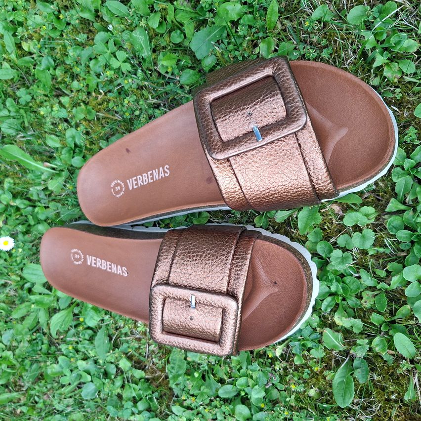 Ein Paar braune Ledersandalen mit einer Schnalle und einer weißen Sohle liegen auf einem grünen Grasfeld.