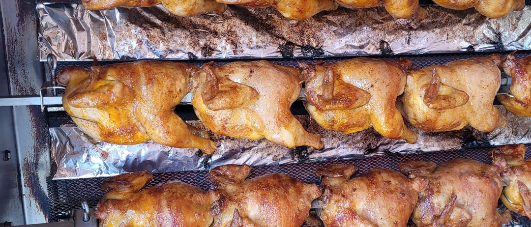 Ein Gestell mit vollständig zubereiteten Hühnern ist zu sehen. Sie haben eine goldbraune Farbe und einige haben rote Markierungen. Sie werden wahrscheinlich für eine Mahlzeit vorbereitet.