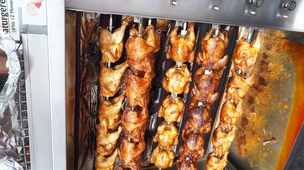 Multiple whole chickens are being cooked on a rotisserie grill, with a golden-brown, crispy skin and a smoky flavor.