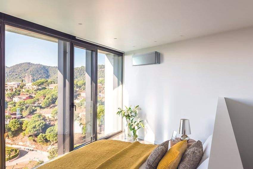 Ein modernes Schlafzimmer mit einem Bett und einem großen Fenster mit Blick auf eine Berglandschaft. Ein Topf mit Pflanzen und eine Lampe stehen auf dem Nachttisch.
