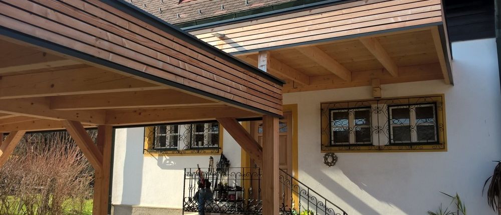 Die Vorderseite eines Hauses mit einer hölzernen Veranda, gelb gestrichenen Wänden und einem hölzernen Vordach. Es gibt zwei Fenster und eine Tür mit schmiedeeisernen Designs.