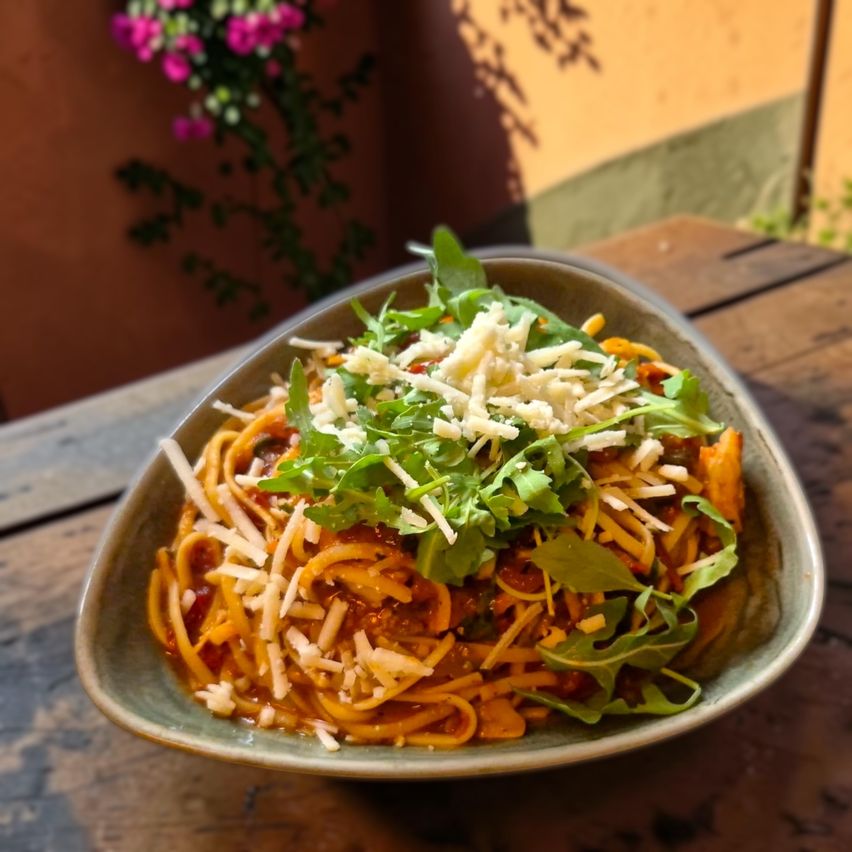 Eine Schüssel mit Spaghetti, Tomatensauce, Käse und Rucola auf einem Holztisch.