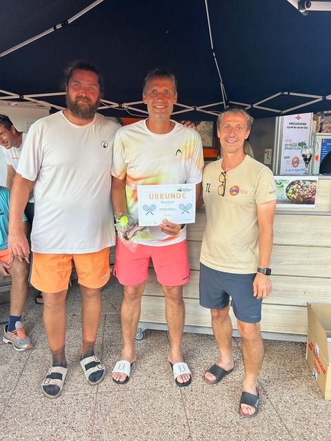 Drei Männer stehen zusammen unter einem Zelt, einer hält ein Zertifikat, ein anderer eine Tennisschläger und einen Tennisball.