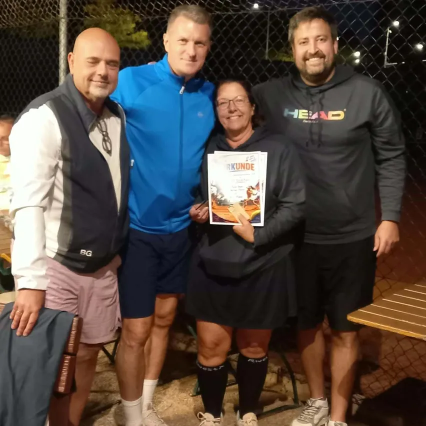 Vier Menschen stehen zusammen, lächeln und posieren für ein Foto. Die Frau in der Mitte hält ein Zertifikat.