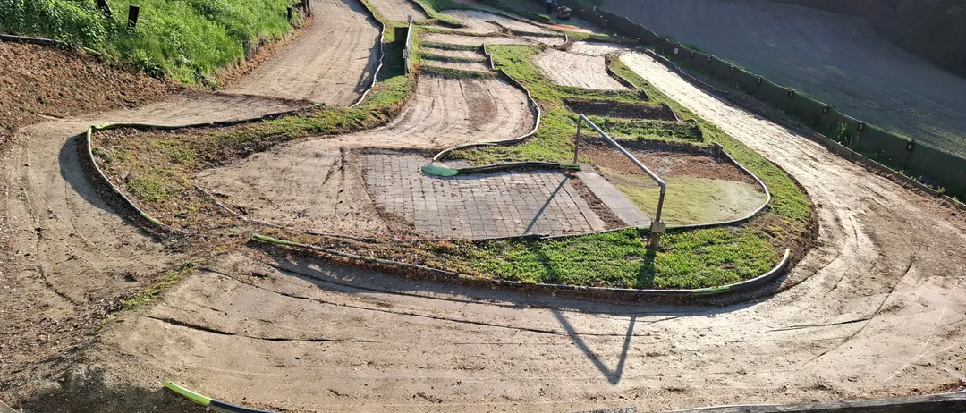Eine Draufsicht auf eine kurvenreiche Erdstrecke mit einem grasbewachsenen Hang auf der linken Seite, einer Betonbarriere auf der rechten Seite und einer Person in der Ferne.