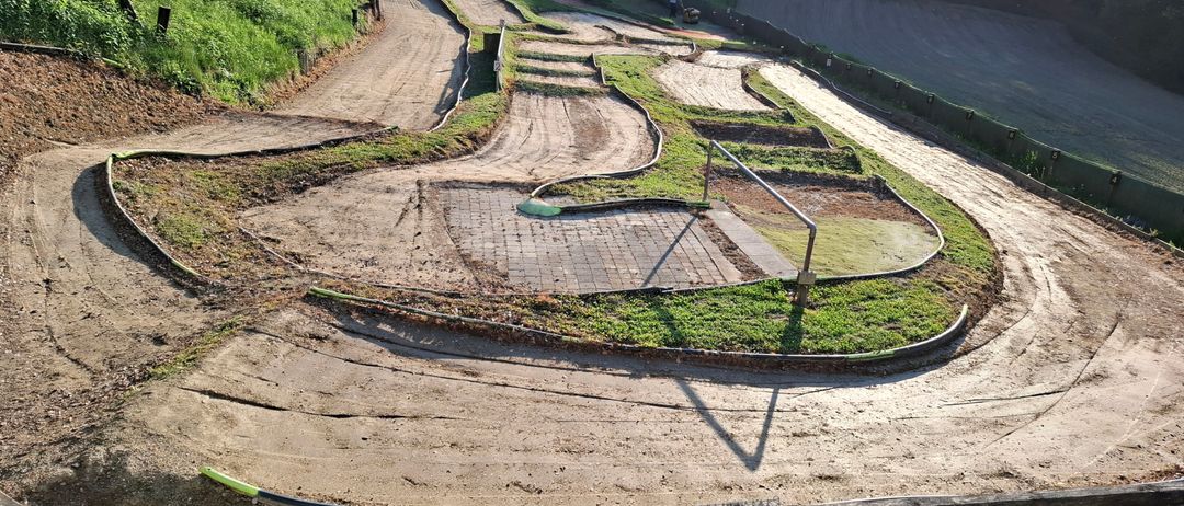 Eine Draufsicht auf eine kurvenreiche Erdstrecke mit einem grasbewachsenen Hang auf der linken Seite, einer Betonbarriere auf der rechten Seite und einer Person in der Ferne.